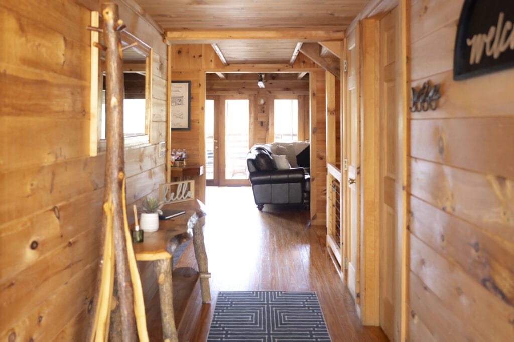 Hallway of the Lincoln Logs Cabin, living room on the other side. In the hallway is a small table with a scent diffuser and a welcome sign
